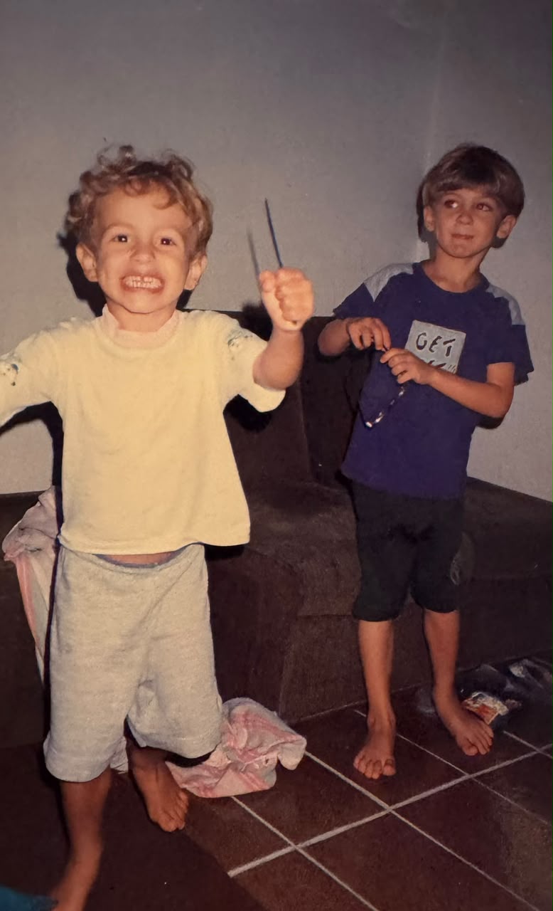 Foto de infância de Eric: dois meninos sorrindo, de pés descalços, dentro de casa