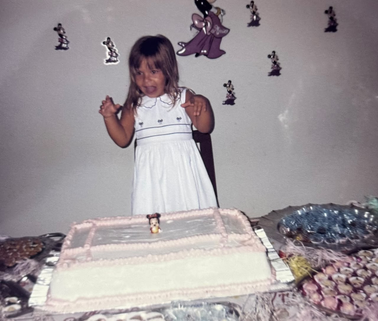 Roberta criança, de vestido branco, em pé diante de um bolo de aniversário