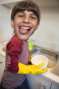 Menino de luvas amarelas lavando louça, rindo